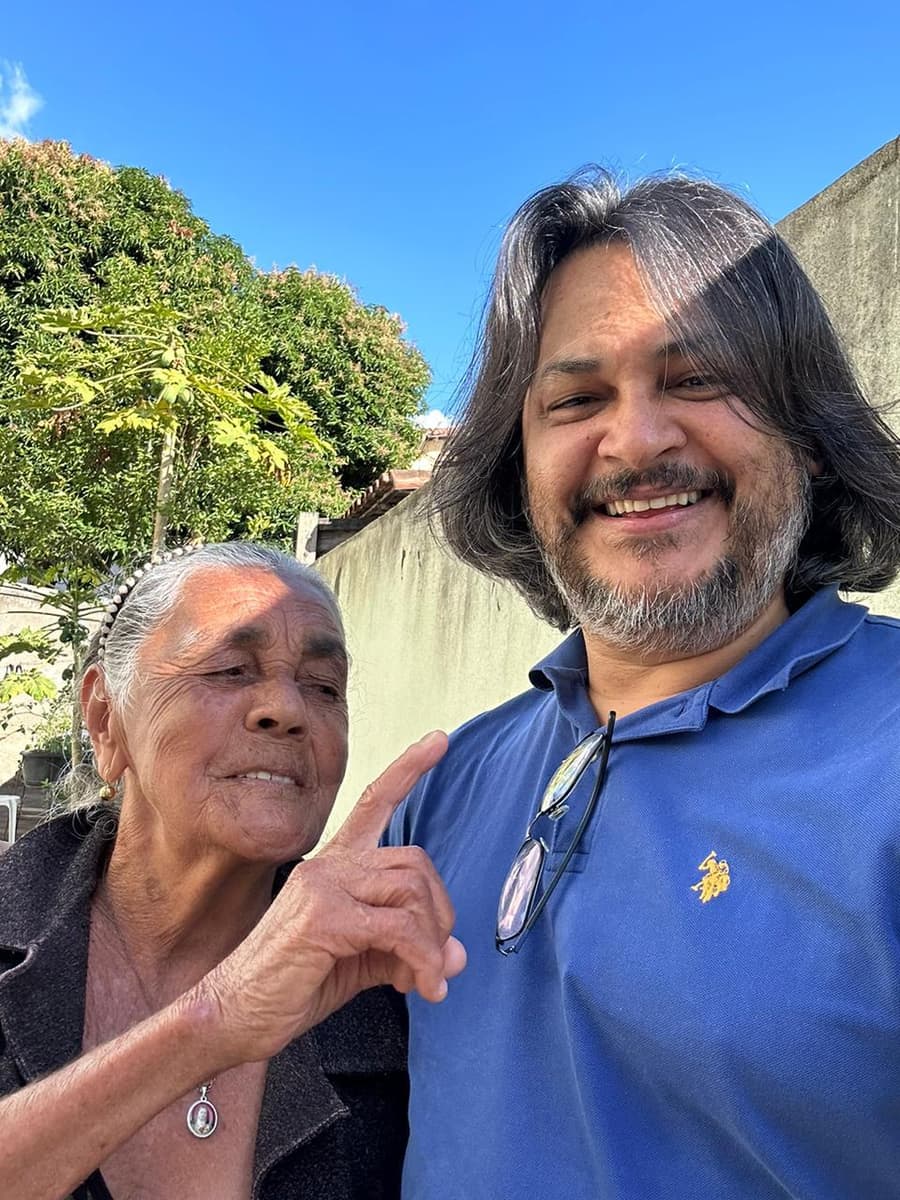 Cézar Ribeiro, sorrindo, abraçado com uma senhora durante uma visita